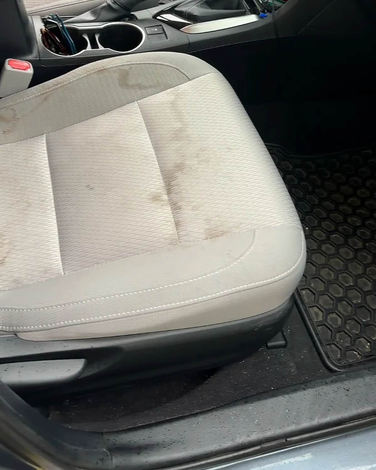 A light grey cloth driver's seat with brown staining across the backrest and cushion
