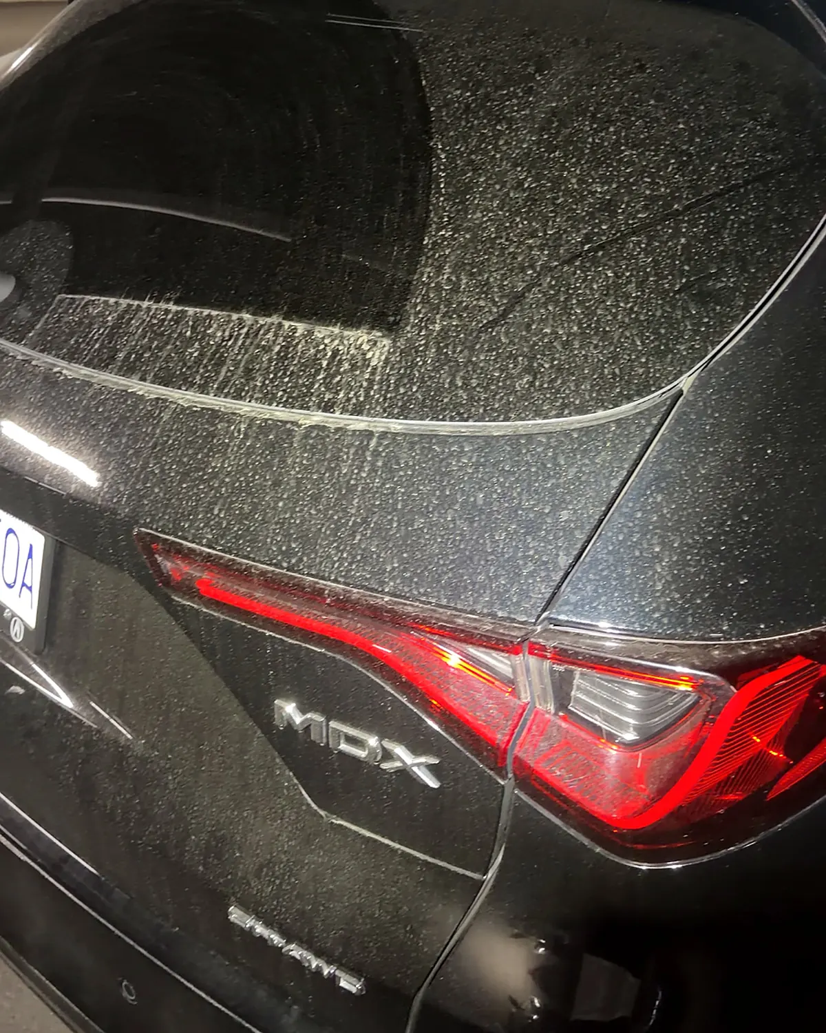 The black rear hatch of an Acura MDX covered in a fine speckle of dried road spray