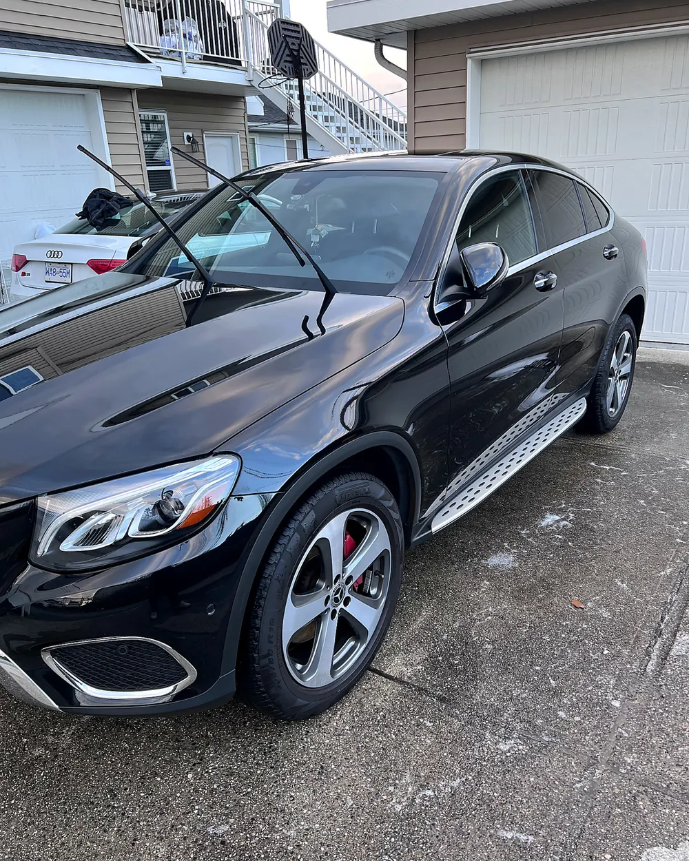 A black Mercedes SUV, just detailed, parked on a driveway beside a garage