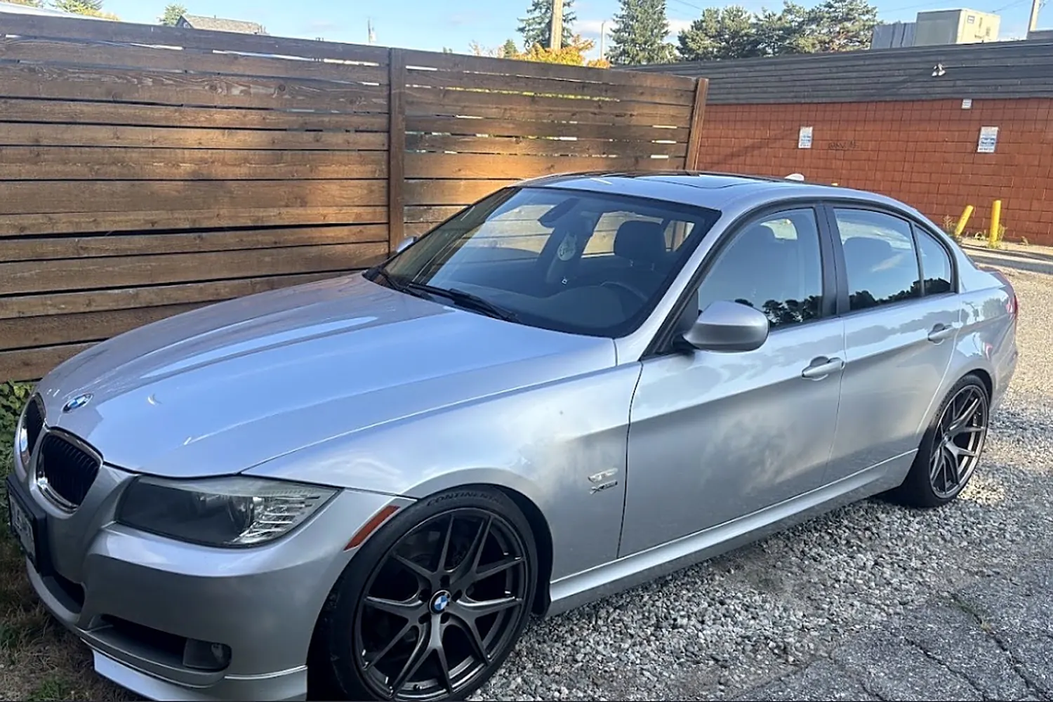 A silver BMW sedan finished and parked on gravel behind a fence