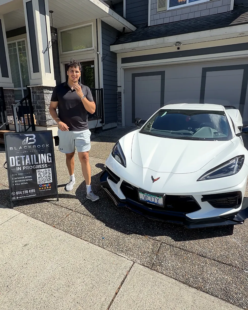 Ed, founder of Blackrock Auto Detail, standing beside a white Corvette on a driveway with the Blackrock “detailing in progress” sign in front of it