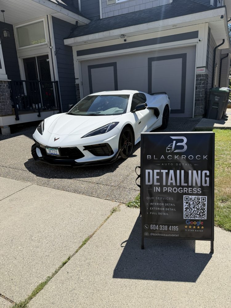 A white Chevrolet Corvette on a driveway beside the Blackrock “detailing in progress” sign